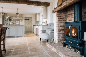A charming rustic kitchen featuring a fireplace, grey cabinetry, and a comfortable armchair.